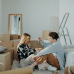 first time home buyers married couple in their living room surrounded by moving vboxes smiling